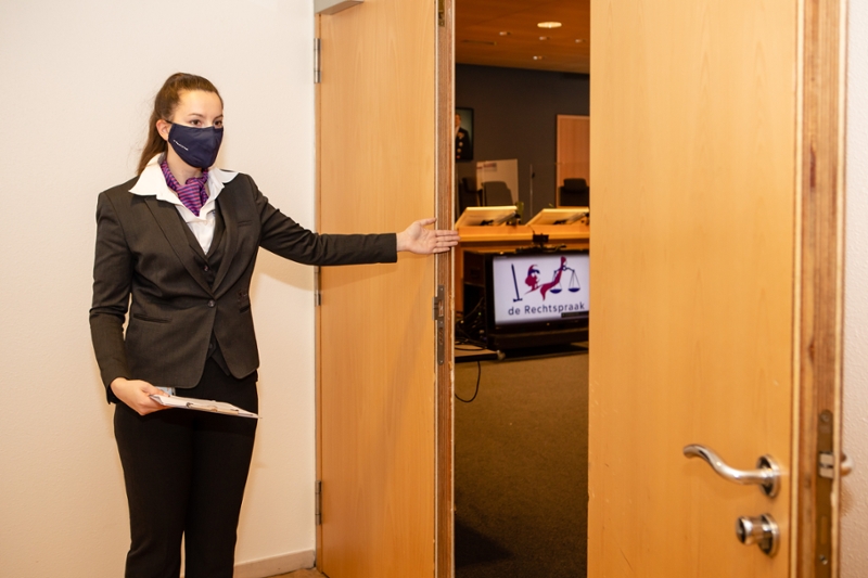Vrouw met mondkapje wijst naar deur rechtszaal